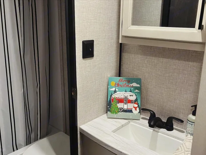 Festive RV rental bathroom with a sink, striped shower curtain, and a camper Christmas sign. Ready for holiday travel.. Highland Ridge RV Open Range 2023