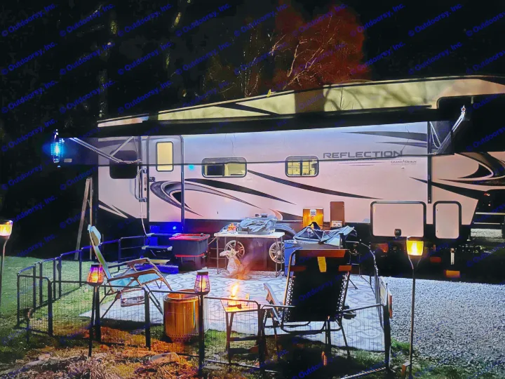 Experience an RV rental: a well-lit camper at night with a glowing fire pit, comfy chairs, and an inviting outdoor area.. Grand Design Reflection 2021