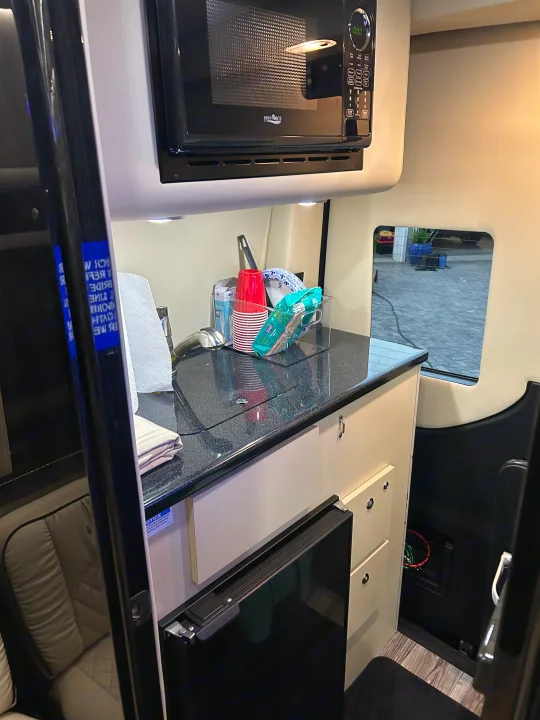 RV rental kitchen: compact area with microwave, sink, counter, and mini-fridge. Ideal for road trip convenience.. Mercedes-Benz Sprinter 2024