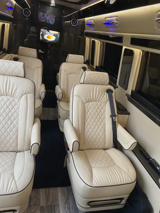 Inside a premium RV rental: comfortable cream leather seating with diamond quilting, sleek dark paneling, and media screens.. Mercedes-Benz Sprinter 2024
