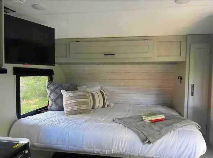 Cozy RV rental bedroom featuring a bed, mounted TV, window view, and overhead storage, perfect for travel.. Forest River Wildwood FSX Plantium 2022