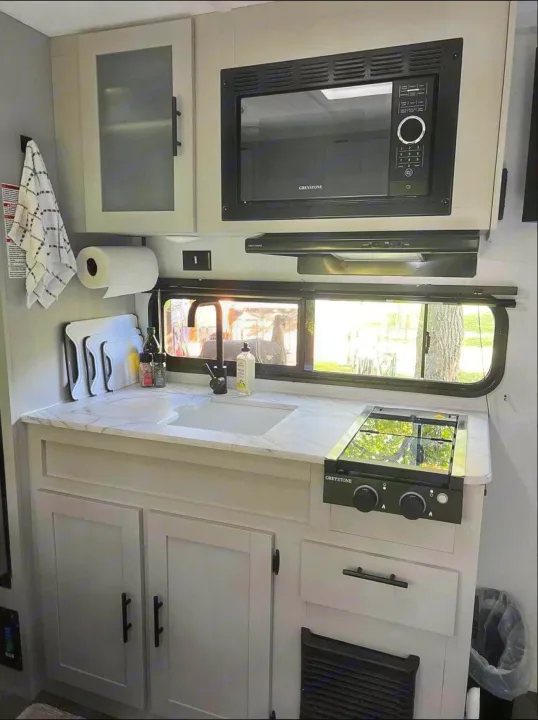 Spacious and modern RV rental kitchen featuring a sink, microwave, stovetop, and ample light from a wide window.. Forest River Wildwood FSX Plantium 2022