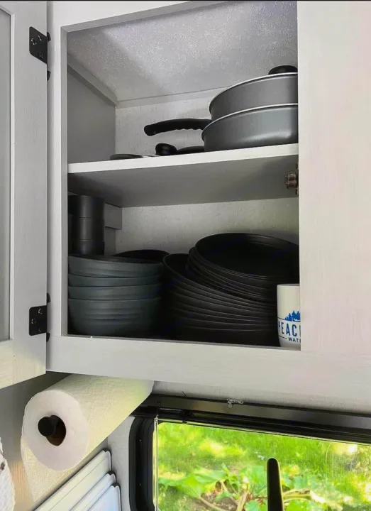 An RV rental kitchen cabinet, showcasing essential cookware, dark dishes, and paper towels for travel convenience.. Forest River Wildwood FSX Plantium 2022