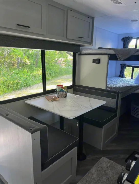 Spacious RV rental featuring a modern dinette, comfy bunk beds, and large windows with outdoor views.. Forest River Wildwood FSX Plantium 2022