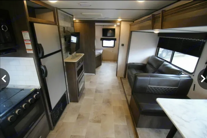 Modern RV rental interior featuring a full kitchen, living area with sofa and dinette, and a glimpse into the bedroom.. Dutchmen Coleman Light 2020