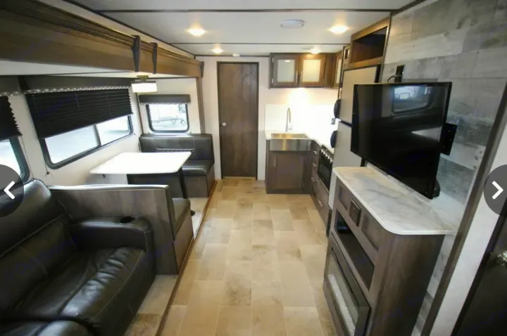 Explore this modern RV rental interior featuring a sofa, dining booth, full kitchen, and entertainment center for your travels.. Dutchmen Coleman Light 2020