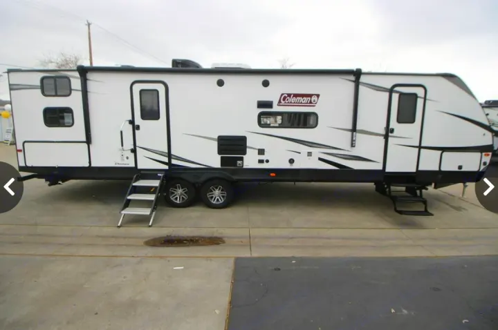 White Coleman travel trailer, a spacious RV rental option, with two entry doors and an awning, parked on concrete.. Dutchmen Coleman Light 2020