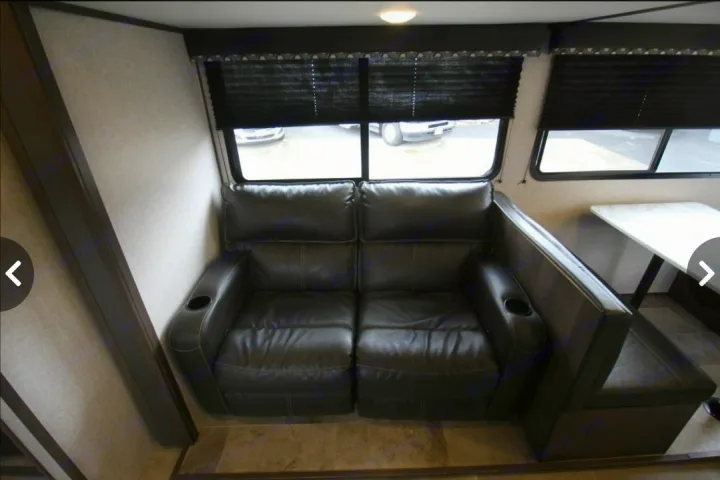 RV rental interior: Black leather loveseat with cup holders, dinette, and windows with blinds for your journey.. Dutchmen Coleman Light 2020