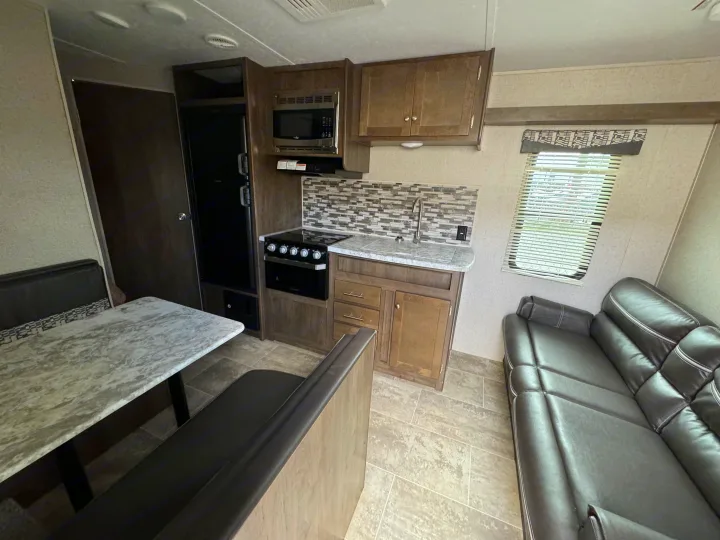 Modern RV rental interior with a compact kitchen (stove, microwave, sink), dining booth, and a comfy leather sofa.. Dutchmen Aspen Trail 2020