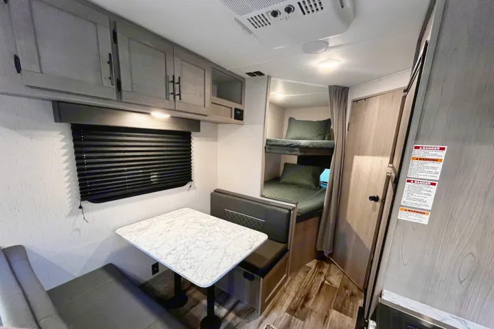 Modern RV rental interior: view of a dinette, sleek bunk beds, and light wood cabinets. Ideal for compact living.. Dutchmen Coleman Lantern 2023
