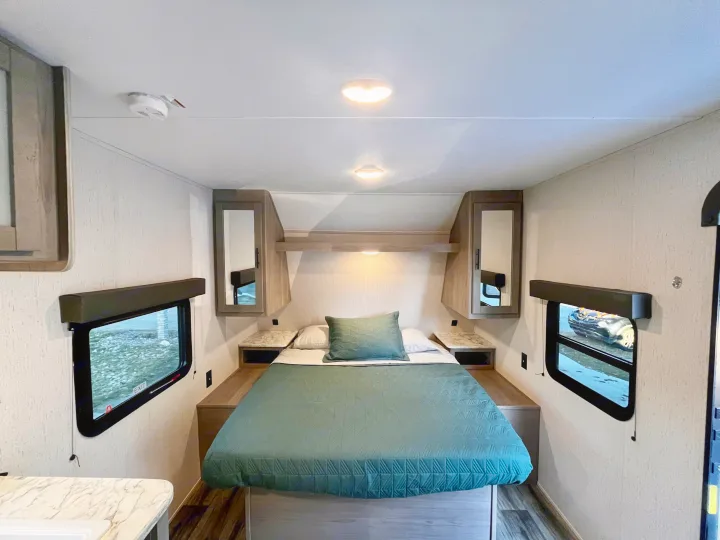 Discover comfort in this RV rental bedroom. Features a cozy bed with green bedding, overhead storage, and natural light from side windows.. Dutchmen Coleman Lantern 2023