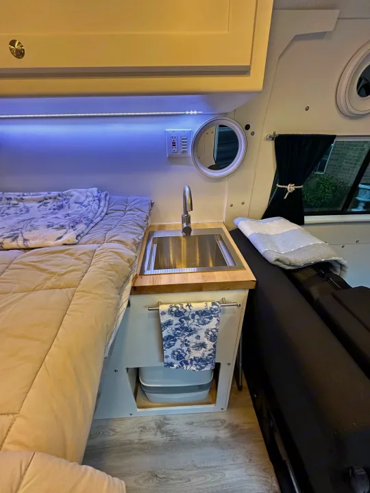 Cozy RV rental interior: bed, sink, and seating area with a view, showing compact living amenities for travelers.. RAM PROMASTER 2500 2023