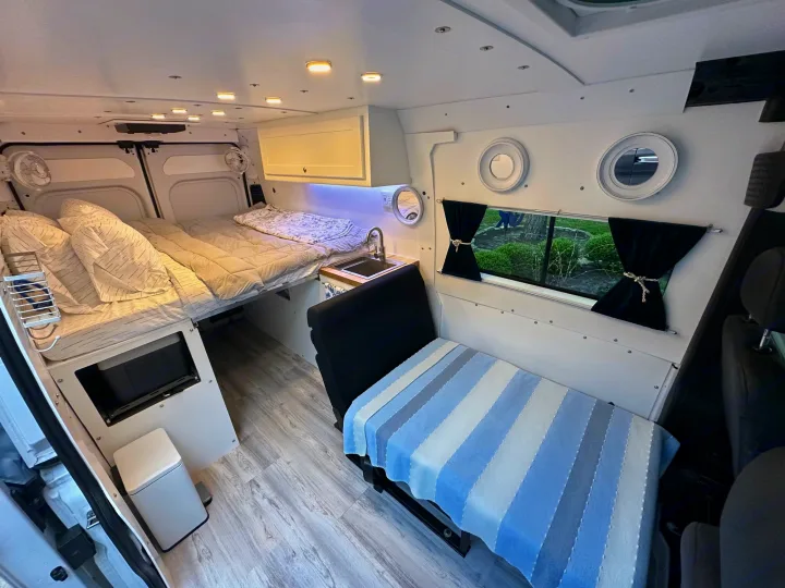 RV rental: Spacious camper van interior with large rear bed, cozy side bench/bed, and compact kitchen area.. RAM PROMASTER 2500 2023