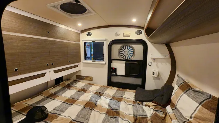 RV rental interior: comfy plaid bed, storage, window, and door. A compact and functional sleeping area for your travels.. Bean Trailer Bean Trailer Trailer 2024