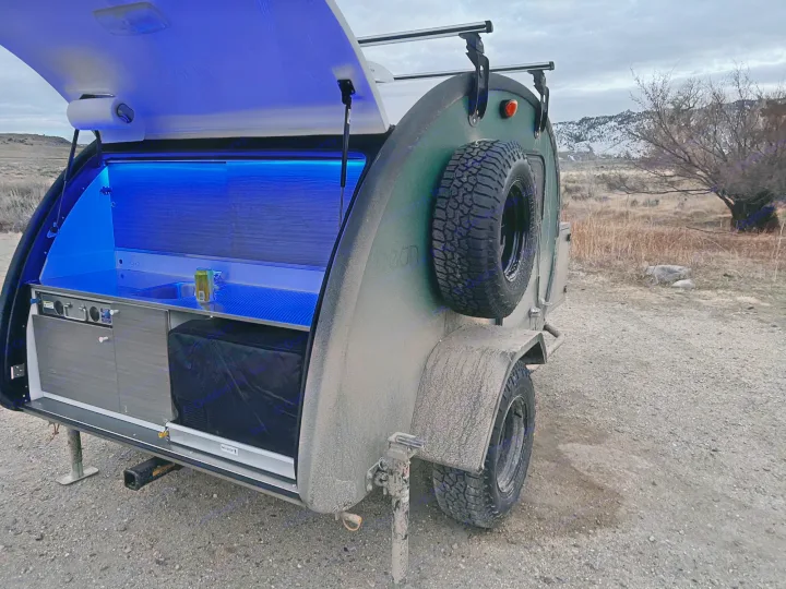 An off-road teardrop camper with a blue-lit outdoor kitchen. Perfect RV rental for rugged adventures.. Bean Trailer Bean Trailer Trailer 2024