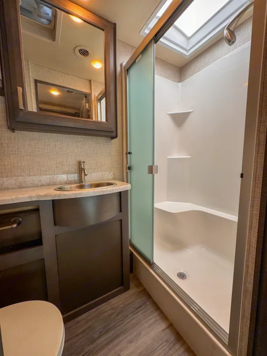 Modern RV rental bathroom: features a spacious shower with skylight and built-in seat, plus a vanity and sink.. Thor Motor Coach Pasadena  Super-C 2023