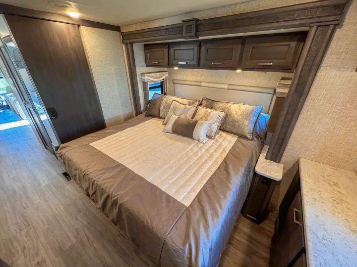 Cozy rv rental bedroom with a large bed, built-in overhead cabinets, and wood flooring. Ideal for comfortable travel.. Thor Motor Coach Pasadena  Super-C 2023