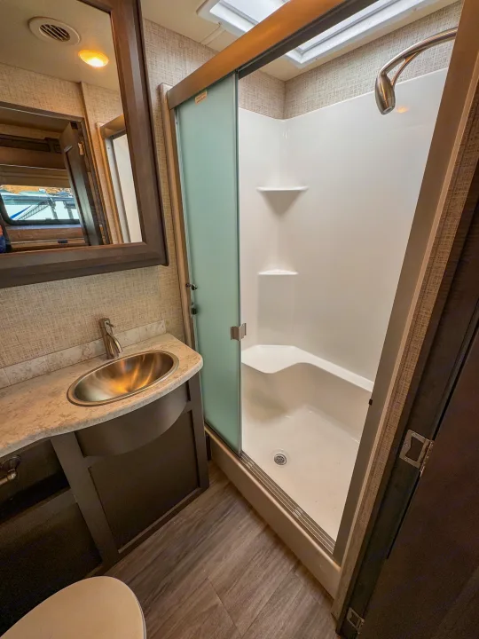 RV rental's compact bathroom: walk-in shower with bench, vanity, sink, and mirror. Efficient mobile living space.. Thor Motor Coach Pasadena  Super-C 2023