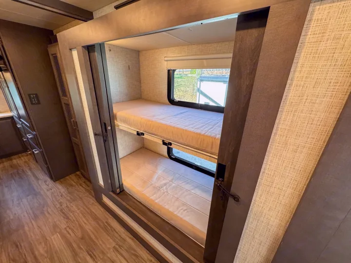Inside this **RV rental**, find two bunk beds with mattresses, windows, and textured walls, offering a cozy sleeping area.. Thor Motor Coach Pasadena  Super-C 2023
