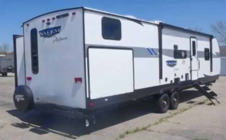 This white travel trailer RV, perfect for your next rv rental, camping, or adventure road trip, is shown from its rear right side.. Forest River Wildwood 2023