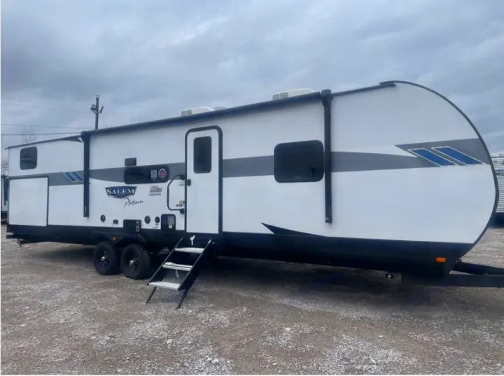 White travel trailer with gray and blue accents, perfect for RV rental. Steps, awning, & multiple windows visible.. Forest River Wildwood 2023