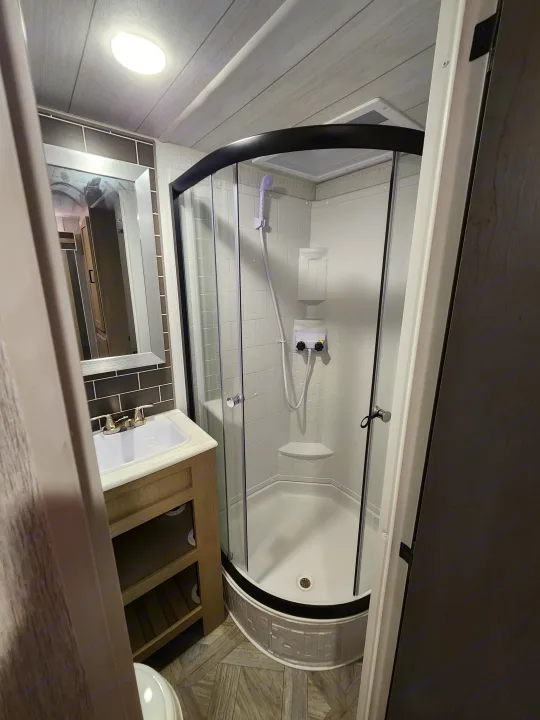Modern RV rental bathroom: curved shower enclosure, vanity, mirror, and light wood accents. Perfect for road trips.. Forest River Wildwood 2023