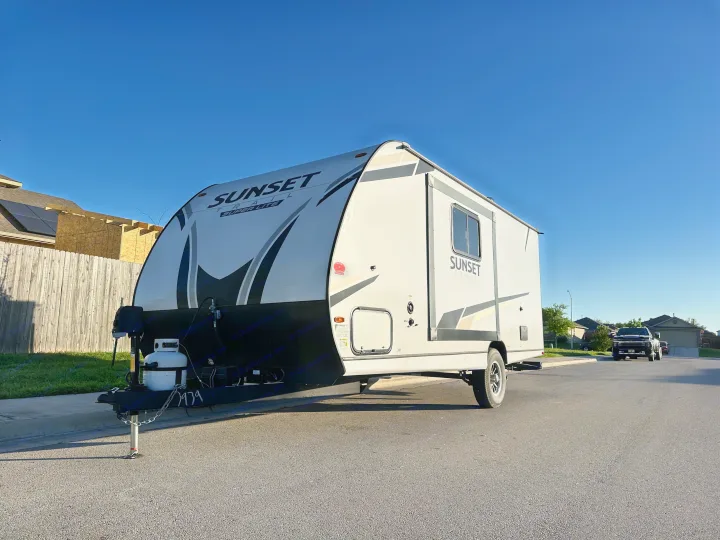 An RV rental, a white Sunset Trail travel trailer, is parked on a residential street under a clear blue sky.. Crossroads RV Sunset Trail Super Lite 2022