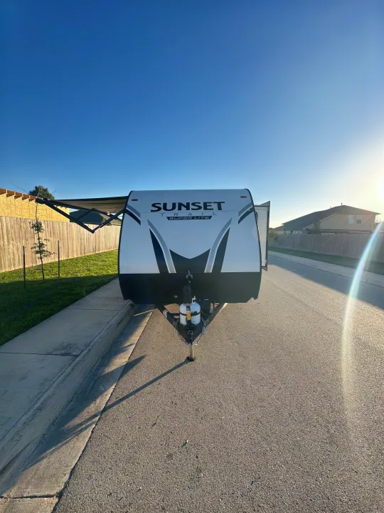 White Sunset Trail Super Lite travel trailer ready for an RV rental, parked on a sunlit street with its awning extended.. Crossroads RV Sunset Trail Super Lite 2022
