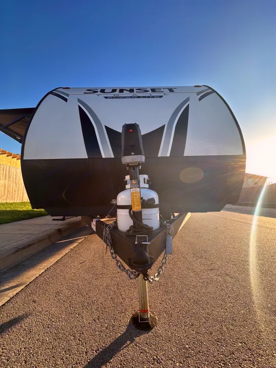 Front view of a Sunset Trail travel trailer, ideal for an RV rental. Visible hitch, propane tanks, and bright blue sky.. Crossroads RV Sunset Trail Super Lite 2022