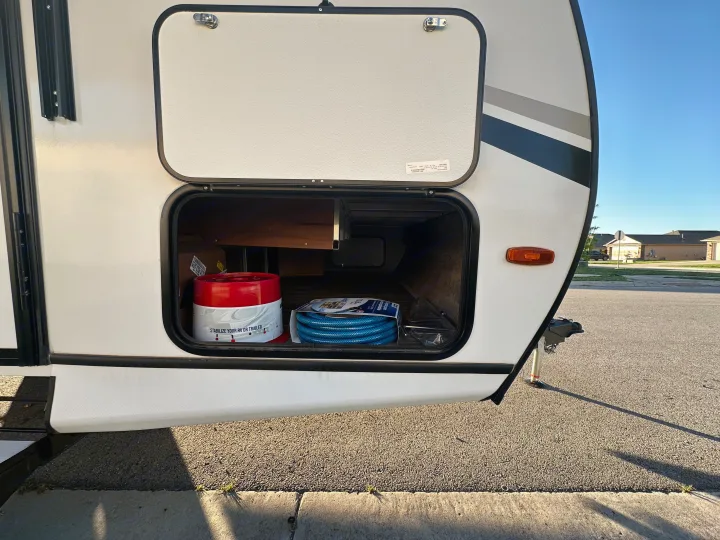 RV rental's side with open external storage. Inside: RV stabilizers and a blue water hose, essential gear for travel.. Crossroads RV Sunset Trail Super Lite 2022