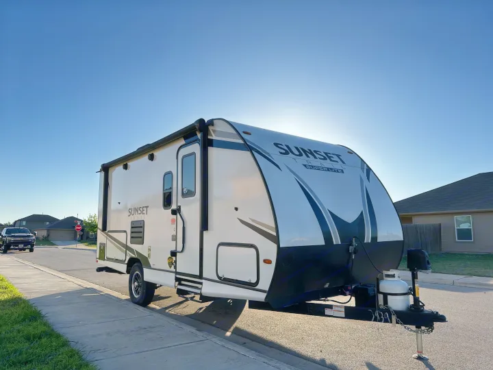 White & black Sunset Trail Super Lite travel trailer RV rental parked on a sunny residential street under a blue sky.. Crossroads RV Sunset Trail Super Lite 2022