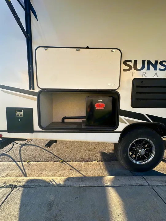 Side view of an RV rental travel trailer with open exterior storage featuring a Hotpoint mini-fridge for outdoor convenience.. Crossroads RV Sunset Trail Super Lite 2022
