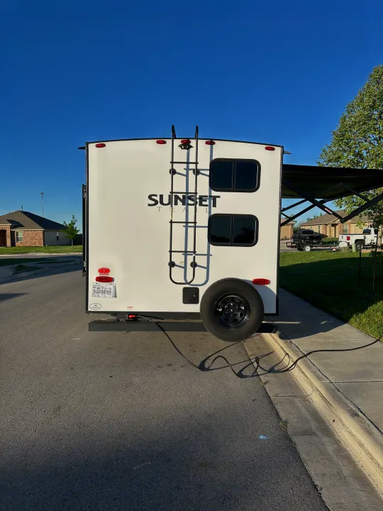 Rear view of a white "Sunset" travel trailer RV rental, featuring a ladder and spare tire. Perfect for road trips.. Crossroads RV Sunset Trail Super Lite 2022