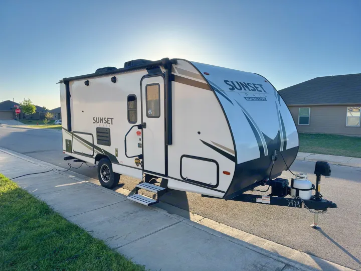 This RV rental: a white Sunset Trail Super Lite travel trailer, parked on a sunny residential street with steps extended.. Crossroads RV Sunset Trail Super Lite 2022