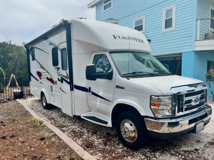 White Forester by Forest River Class C RV rental parked on gravel next to a light blue house.. Forester GTS 2018