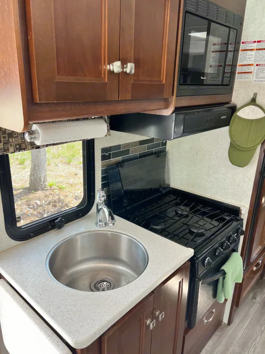 This RV rental kitchen features a stainless sink, gas stove, microwave, and wooden cabinets, perfect for compact living.. Forester GTS 2018