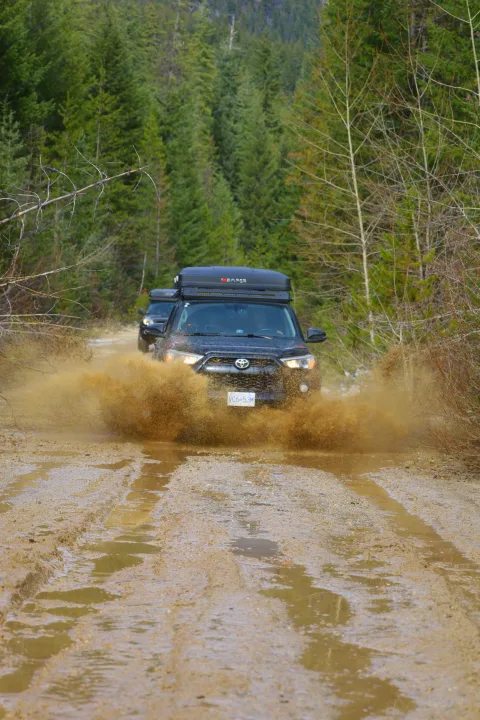 Black SUV with rooftop tent (like an RV rental) splashes mud on a forest trail. Off-road adventure vehicle in action.. Toyota Other 2015
