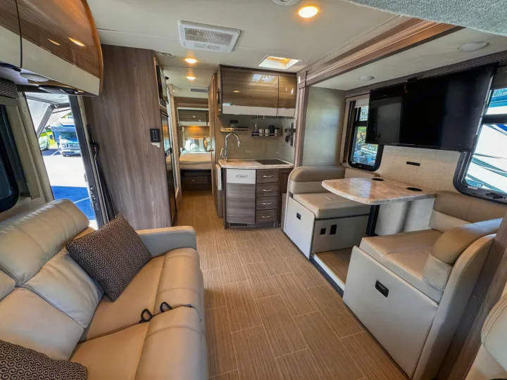 Spacious, modern RV rental interior with light wood accents, showing living room, kitchen, and bedroom for comfortable travel.. Thor Motor Coach Delano 2022