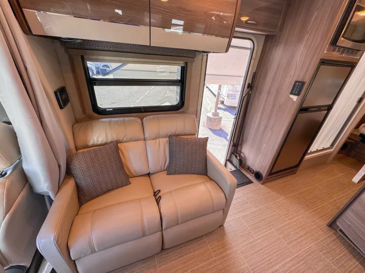 Spacious RV rental interior with light leather sofa, large window, wood cabinets, and kitchen appliances.. Thor Motor Coach Delano 2022