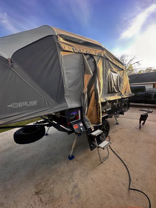 An OPUS Off-Road pop-up RV set up on concrete. This off-road rv rental unit's tent is extended, with steps and a dog.. OPUS Opus4 2024