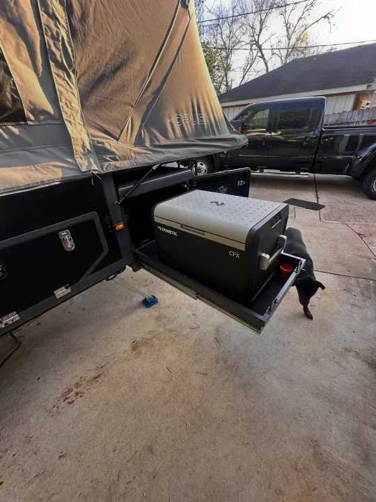 Pop-up Opus camper with Dometic fridge pulled out on a slide, ideal for RV rental adventures. A dog and truck are nearby.. OPUS Opus4 2024