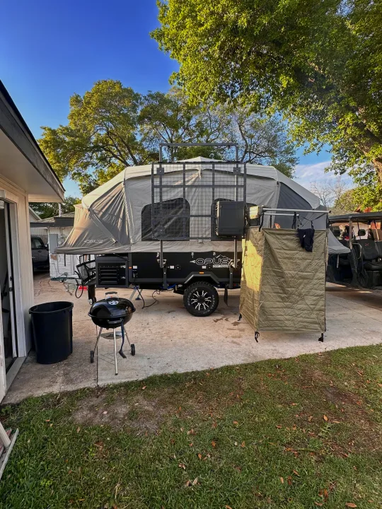 Opus Off-Road pop-up trailer set up on a patio with a grill, perfect for your next rv rental adventure.. OPUS Opus4 2024