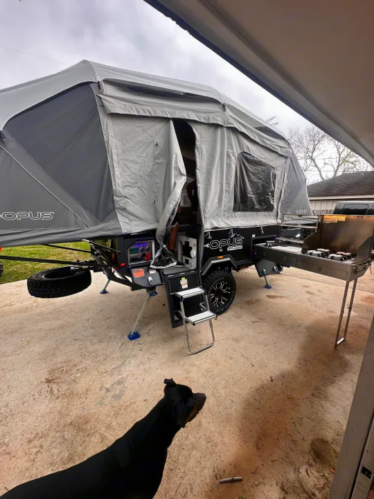 OPUS Off-Road pop-up camper with outdoor kitchen, ready for your RV rental adventure. A black dog is visible in the foreground.. OPUS Opus4 2024