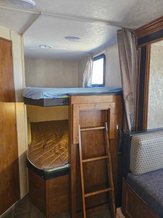 Cozy RV rental interior featuring bunk beds, a ladder, and a patterned dinette seating area, ideal for family trips.. Forest River Salem Cruise Lite 2017