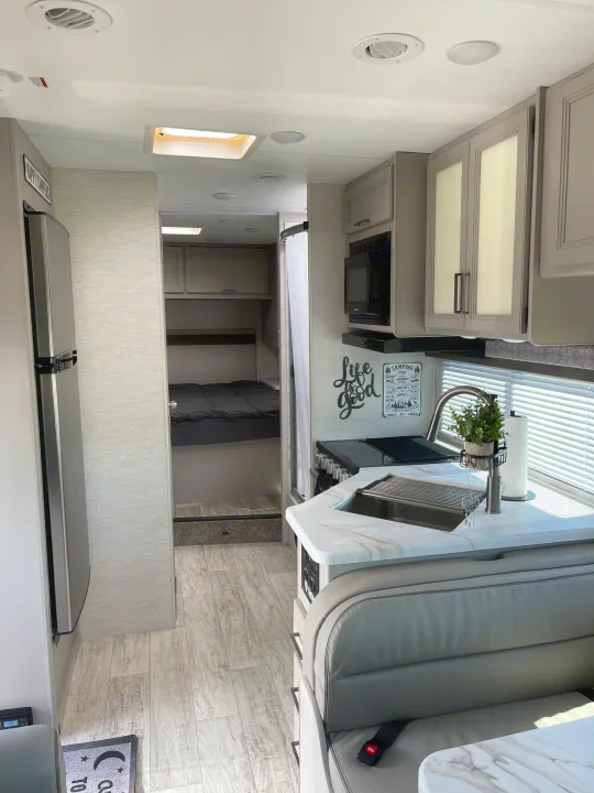 Spacious RV rental interior: modern kitchen, comfortable dining area with seating, and a cozy bedroom in the back.. Thor Motor Coach Chateau 2024