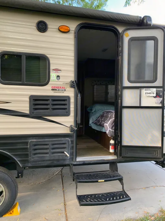 Side view of an RV rental with its door open, revealing interior bed, steps, and exterior features like vents. Ready for travel!. Coachmen Clipper 2017
