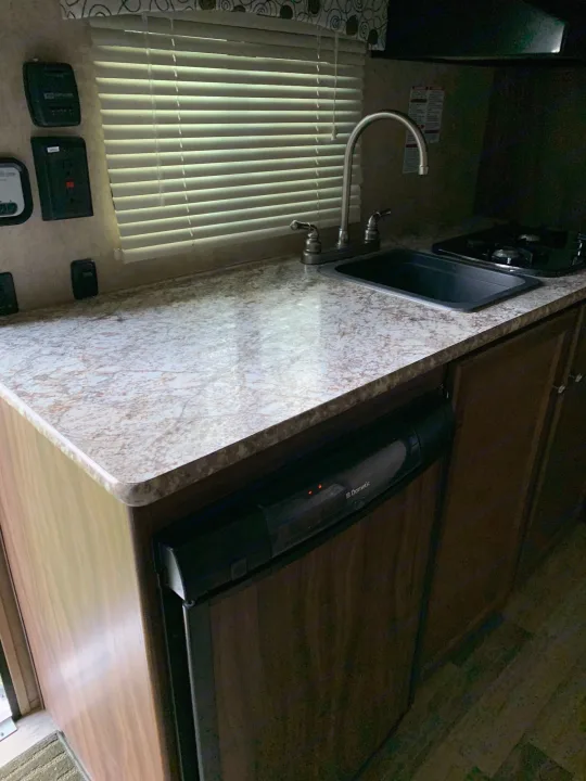 RV rental's compact kitchen: sink, two-burner stove, Dometic fridge, and light mottled countertop.. Coachmen Clipper 2017