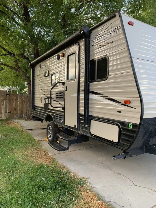 This travel trailer, available as an rv rental, is parked on a driveway beside a fence and tree.. Coachmen Clipper 2017