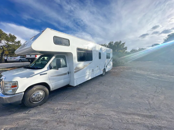 White Class C RV rental parked on a dirt lot under a bright, cloudy sky. Perfect for a road trip adventure.. Thor Majestic 2016