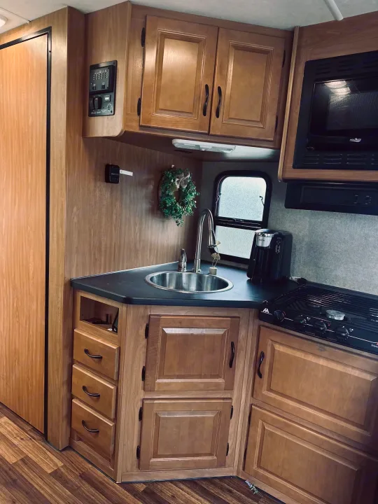 Inside an RV rental, a functional kitchen with light wood cabinets, dark counters, sink, microwave, and stove.. Thor Majestic 2016